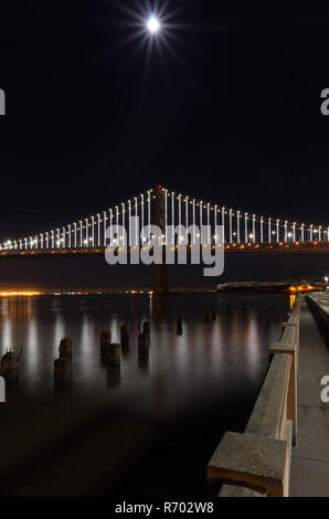 L'article de Bay Bridge éclairés la nuit avec la pleine lune et la réflexion sur l'eau de la baie de San Francisco, CA Banque D'Images