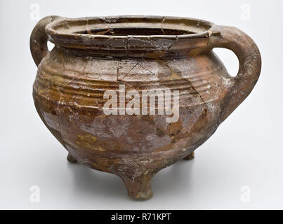 Raisin poterie, casserole avec ventre rond, trois pieds et deux oreilles, raisin de table ustensiles de cuisine porte-pot en faïence céramique faïence glaze glaçure de plomb à la main, émaillés de poterie cuite tourné sur trois pieds de raisin. Ventre en forme de balle et deux oreilles dépasser légèrement au-dessus du bord. Décorées avec des rotations sur l'épaule. L'Écharde de rouge en partie recouvert de plomb glaçure. Et en circulation à profil haut avec couvercle emplacement situé à l'intérieur d'archéologie Heenvliet Bernisse poteries indigènes cuisine cuisson préparation alimentaire sol nutrition : Pastorieterrein Heenvliet découverte vlak. Banque D'Images