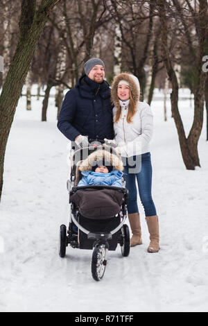 Happy Family walking dans le parc en hiver. Les parents portent le bébé dans une poussette à travers la neige. Banque D'Images