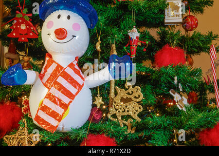 Grand bonhomme gonflable sur un arbre de Noël. Air soufflé la figure de saison devant un arbre de Noël artificiel éclairé avec des lumières et des décorations. Banque D'Images