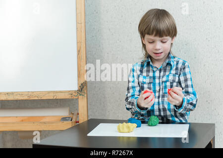 Garçon Blond sculpte à partir de pâte à modeler à la maison à la table. L'idée et concept de l'école, l'école, la maison de l'éducation et activités de développement. Banque D'Images