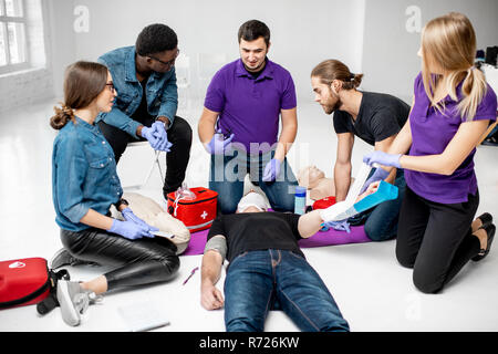 Groupe de jeunes au cours de la formation en premiers soins avec moniteur montrant comment appliquer un bandage sur la personne lésée Banque D'Images