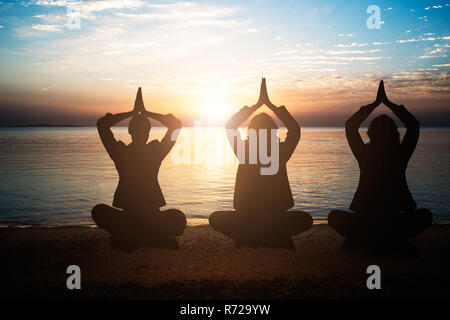 Silhouette de personnes méditant au Beach pendant le coucher du soleil Banque D'Images