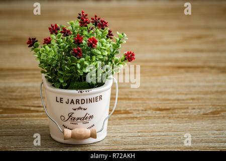 Fleur rouge artificiel en pot blanc sur fond de bois Banque D'Images