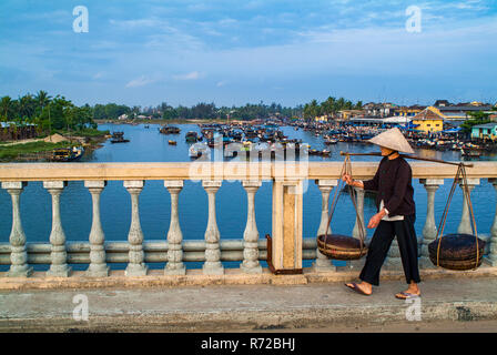 Vieille Femme portant un joug chargées traversant une rivière à Hoi An, Vietenam Banque D'Images