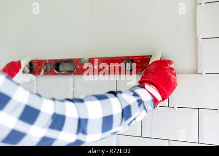 Processus de carrelage les carreaux dans la cuisine. Niveau de mesure de la construction de l'entrepreneur avec niveau sur les carreaux muraux, outils de mesure. Amélioration de l'habitat, de rénovation concept. Banque D'Images