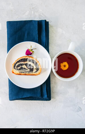 Tranche de pavot Graines roll servi sur une assiette et une tasse de thé de fleurs sur un fond noir en blanc. Banque D'Images
