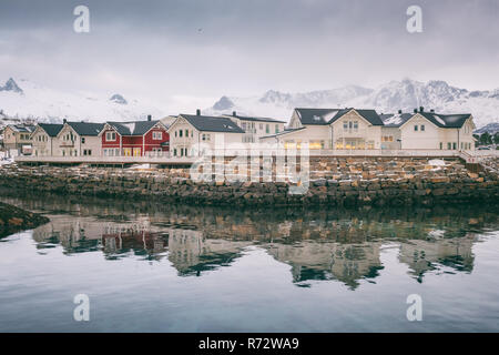 Paysage d'hiver avec des maisons blanches et rouges, reflet dans l'eau et la neige des montagnes, Kabelvag, îles Lofoten, Norvège Banque D'Images