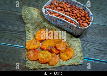 Abricots séchés et d'arachides dans un panier en osier sur une table en bois close-up Banque D'Images