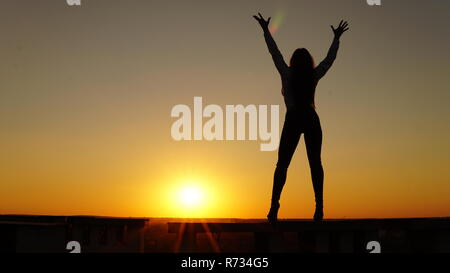 Jeune fille en uniforme de sport se trouve sur le bord du toit pendant le coucher du soleil Banque D'Images