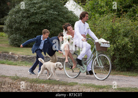 Les jeunes invités du mariage à courir après les nouveaux mariés sur les bicyclettes Banque D'Images