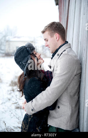 Jeune couple hugging contre chalet dans la neige Banque D'Images