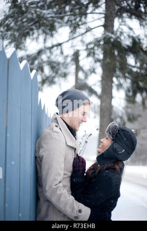 Jeune couple hugging against fence in snow Banque D'Images
