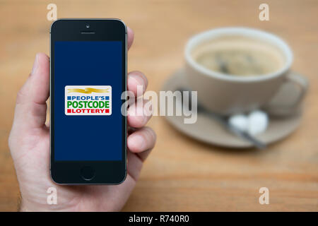 Un homme se penche sur son iPhone qui affiche la Postcode Lottery logo (usage éditorial uniquement). Banque D'Images