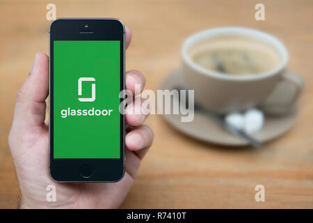 Un homme se penche sur son iPhone qui affiche le logo Glassdoor (usage éditorial uniquement). Banque D'Images