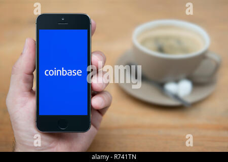 Un homme se penche sur son iPhone qui affiche le logo Coinbase (usage éditorial uniquement). Banque D'Images