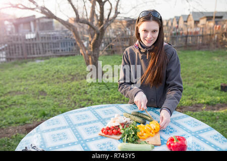 Happy young woman cutting légumes frais sur une table à l'extérieur dans le jardin Banque D'Images