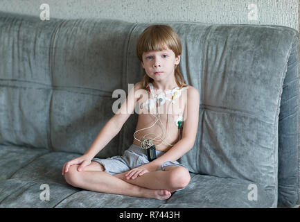 Enfant assis sur le canapé. Cardiogramme ou la surveillance de la fréquence cardiaque de la performance cardiaque en utilisant le Holter. Banque D'Images