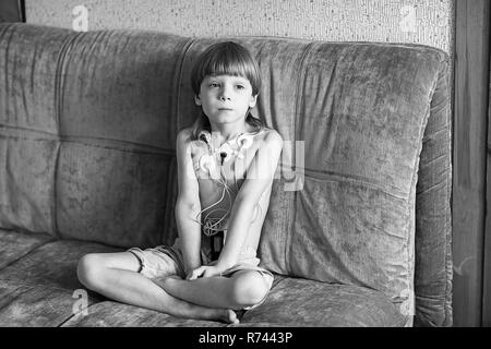 Enfant assis sur le canapé. Cardiogramme ou la surveillance de la fréquence cardiaque de la performance cardiaque en utilisant le Holter. Banque D'Images