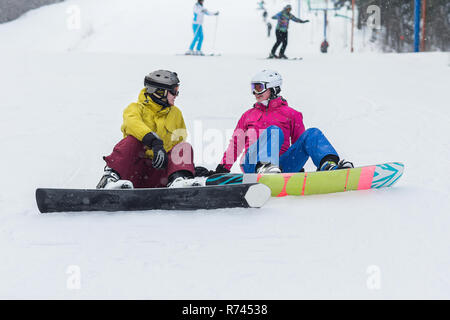 Jeune couple assis sur la pente de planche sur une journée d'hiver. Couple heureux les athlètes. Banque D'Images