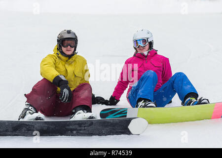 Jeune couple assis sur la pente de planche sur une journée d'hiver. Couple heureux les athlètes. Banque D'Images