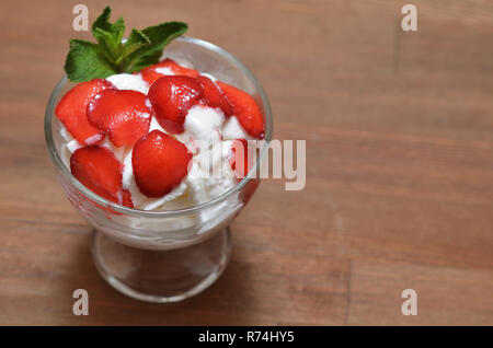 Crème glacée à la vanille avec des fraises et des feuilles de menthe dans un bol en verre. Banque D'Images