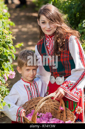 La femme vêtue d'un costume folklorique traditionnel bulgare picking roses dans un jardin, dans le cadre de l'été World rituel dans vallée des Roses, en Bulgarie. Banque D'Images