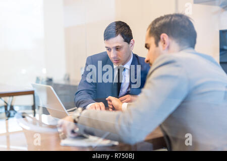 Deux jeunes hommes d'utiliser un ordinateur portable lors de réunions d'affaires. Banque D'Images