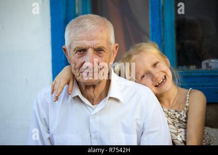 Petite-fille embrassant avec grands parents assis à l'avant de la maison rurale Banque D'Images