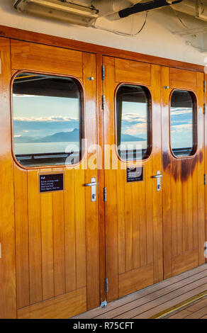Vernis en bois lourds portes extérieures avec windows et réflexions de mer et soleil du matin dans des panneaux de verre sur un bateau de croisière. L'Alaska, USA. Banque D'Images