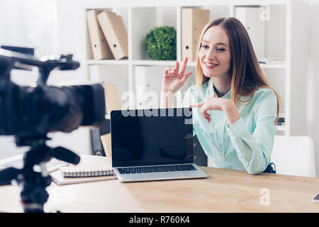 Smiling attractive female video blogger vlog enregistrement dans office, ordinateur portable avec écran vide sur la table d'examen Banque D'Images