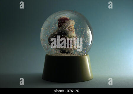 Le Père Noël porte un sac sur son dos une marche dans une tempête de neige dans un globe. Isolé sur fond bleu. Banque D'Images