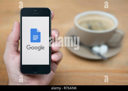 Un homme se penche sur son iPhone qui affiche le logo de Google Docs (usage éditorial uniquement). Banque D'Images