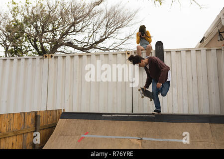Femme photo tout en cliquant skateur skateur mâle patinage sur la rampe de planche à roulettes Banque D'Images