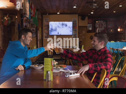 Friends toasting beer glasses in pub Banque D'Images