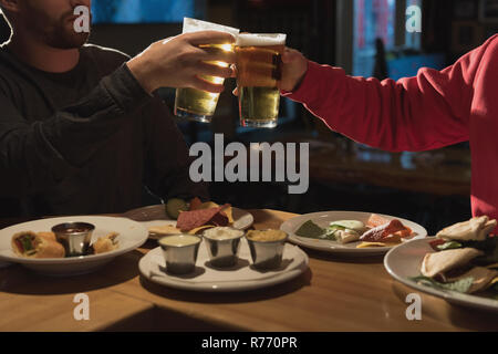 Friends toasting beer glasses in pub Banque D'Images