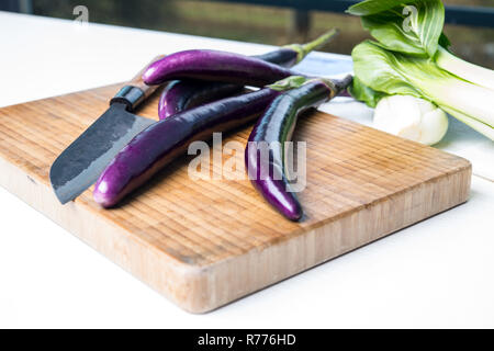 Aubergine japonaise sur planche de bois avec couteau et salade de pak choi Banque D'Images