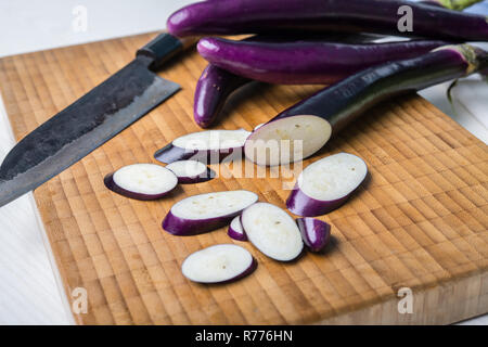 Aubergine japonaise sur planche de bois avec couteau et salade de pak choi Banque D'Images