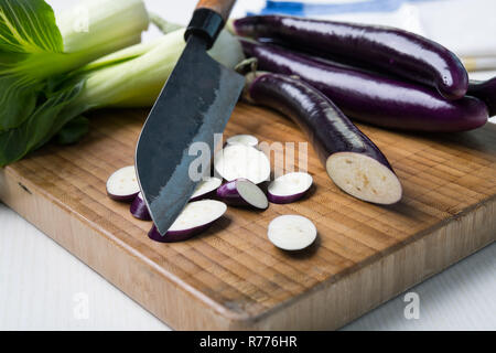 Aubergine japonaise sur planche de bois avec couteau et salade de pak choi Banque D'Images