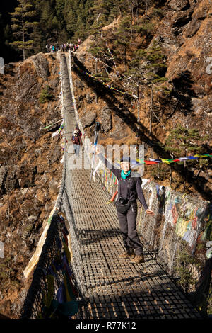 Le Népal, Larja Dobhan, senior woman holding up pôles trekking célébrant la région de passage Larja pont suspendu au-dessus de la rivière Dudh Sculpture khosi Banque D'Images