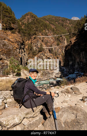 Le Népal, Larja Dobhan, senior woman sur Everest Base Camp Trek, reposant à côté de la rivière Dudh Sculpture khosi à Larja supérieur et inférieur des ponts Banque D'Images