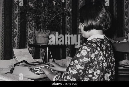 Années 1970, jeune fille en fleur un top à motifs assis à un bureau taper ses notes soigneusement sur une petite machine à écrire manuelle, England, UK. Banque D'Images