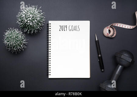 Les résolutions du nouvel an 2019 télévision sport composition laïcs. Haltères en noir, blanc, bande de mesure portable et mini arbre de Noël sur fond noir. Banque D'Images