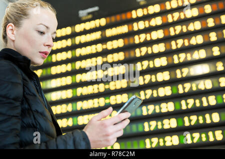 Femme à l'aéroport en face du conseil d'information de vol de contrôle de son téléphone. Banque D'Images