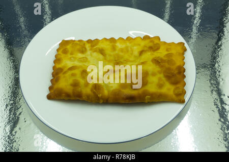 L'ouzbek cuisine tatare, cheburek avec de la viande et des fromages suluguni dans une plaque blanche avec des légumes verts et sur une table en bois Banque D'Images