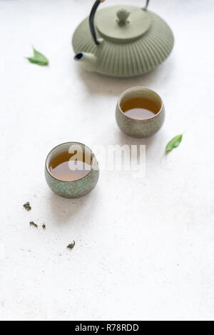 Service à thé asiatique - théière en céramique et de tasses de thé avec du thé vert. La composition traditionnelle du thé sur fond blanc, copie de l'espace. Banque D'Images