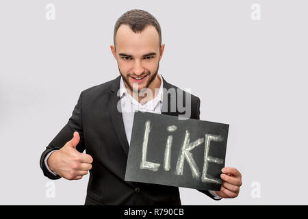Jeune homme positif et tenir stand comprimé avec de l'écrit comme. Il montre son gros pouce vers le haut. Guy porte de même. Isolé sur fond blanc. Banque D'Images