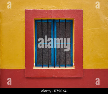 Mur minimaliste image d'une seule fenêtre bleu, centré avec barres de protection, encadré en rouge sur un mur jaune Banque D'Images