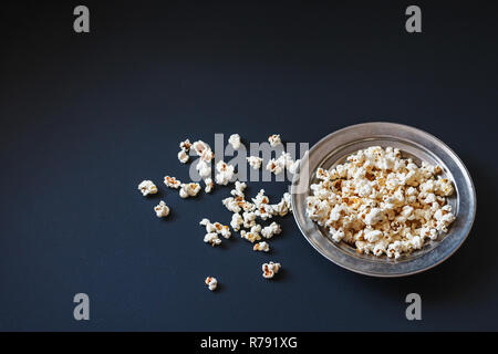 Vue de dessus de popcorn dans une plaque métallique sur une surface noire mate. Savoureuse source de fibres alimentaires. Banque D'Images