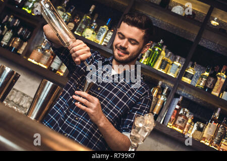 Jeune barman debout à comptoir bar alcool en versant jigger heureux Banque D'Images